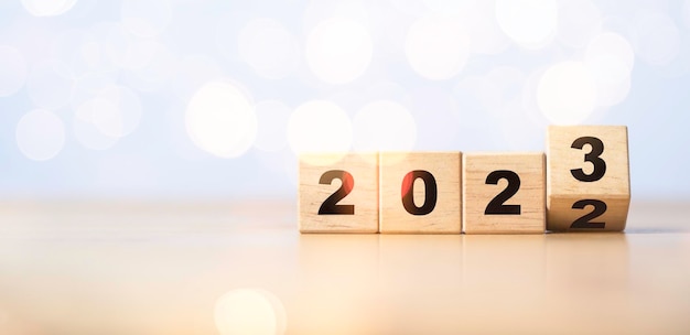 Voltear el cubo de bloques de madera para cambiar 2022 a 2023 con bokeh para el concepto de preparación de feliz Navidad y feliz año nuevo