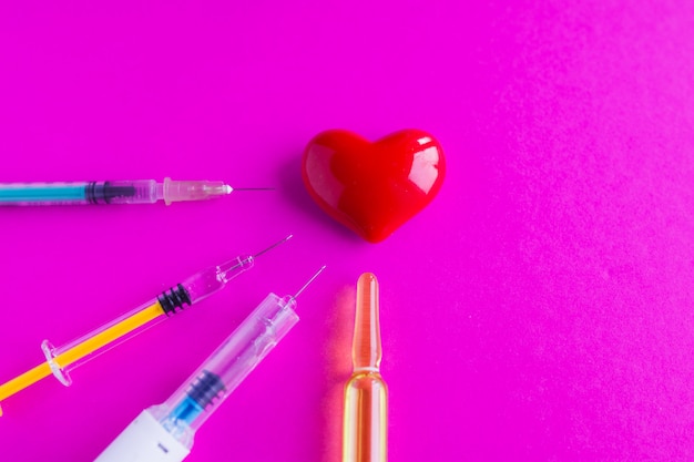 volumetrisches Herz mit Spritzen auf einem rosa Hintergrund. Das Konzept der Unterstützung von Patienten mit Herzerkrankungen