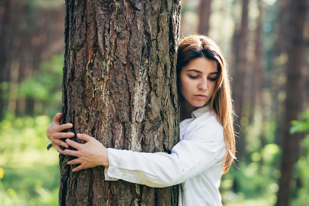 Voluntaria hermosa joven abraza un árbol con amor en el bosque