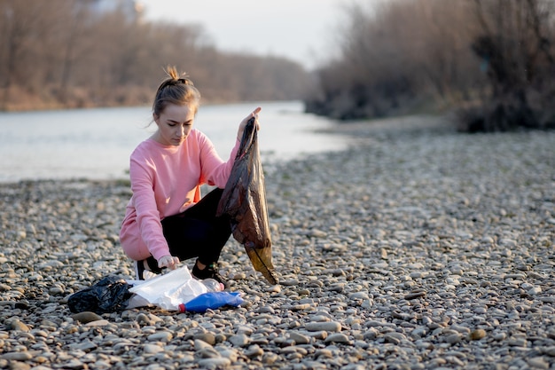 Voluntaria joven recogiendo basura junto al río