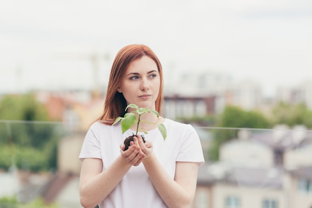 Voluntária segura nas mãos uma muda de uma árvore de flores