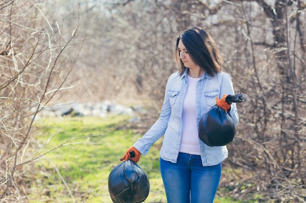 Voluntaria sostiene bolsas con plástico recolectado limpiando el bosque y el parque de basura