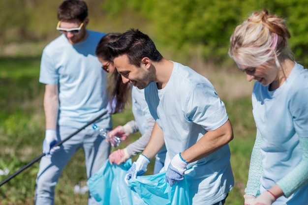 voluntariado, caridade, limpeza, conceito de pessoas e ecologia - grupo de voluntários felizes com área de limpeza de sacos de lixo no parque