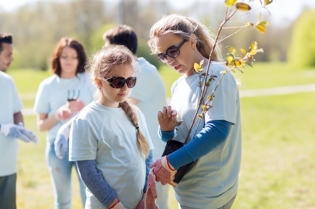 voluntariado, caridade, pessoas, família e conceito de ecologia - mãe e filha são voluntárias com mudas de árvores no parque
