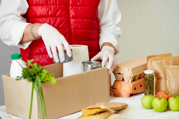 Voluntarie-se na máscara médica protetora e luvas colocando alimentos na caixa de doação.