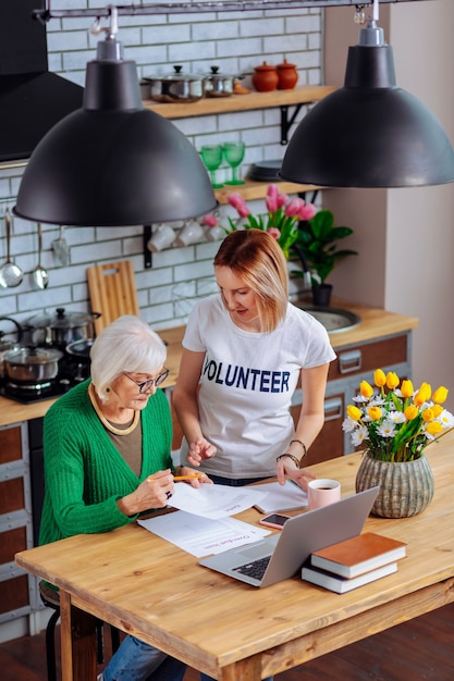 Voluntario adulto joven discutiendo con una anciana en la cocina