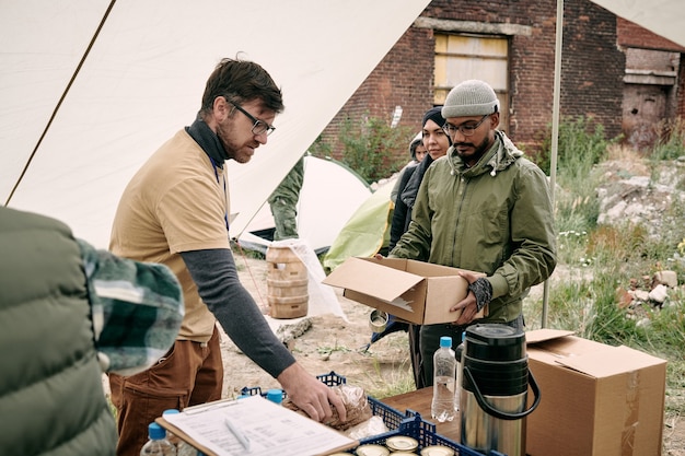 Voluntário barbudo com camiseta amarela em pé em uma barraca de comida dando comida aos refugiados
