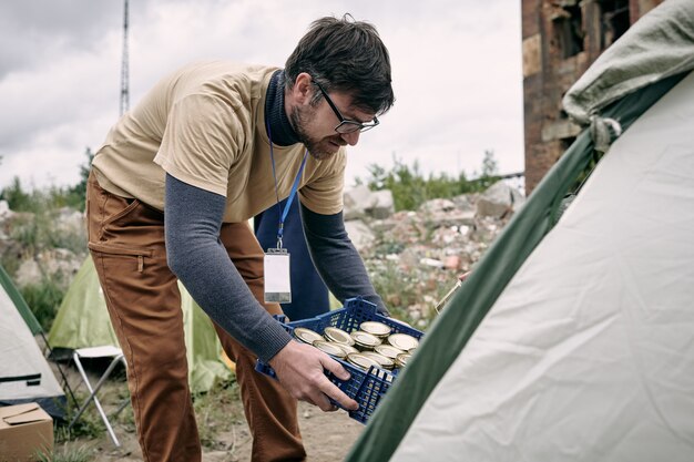 Voluntário do sexo masculino com caixa de comida enlatada dobrando-se na barraca