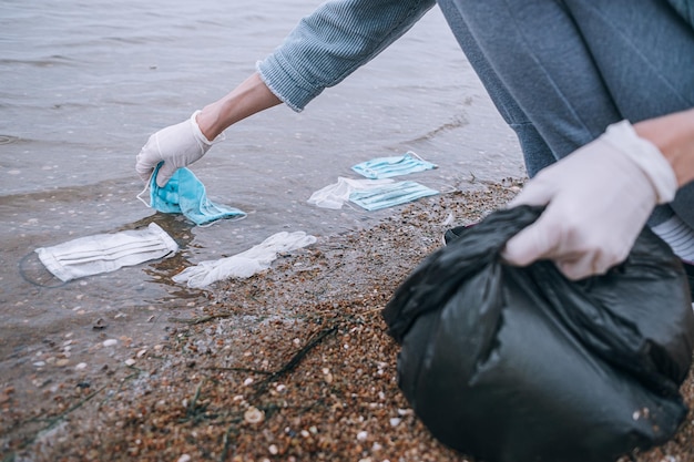 Voluntário feminino remove detritos de máscaras e luvas médicas usadas na praia e na água