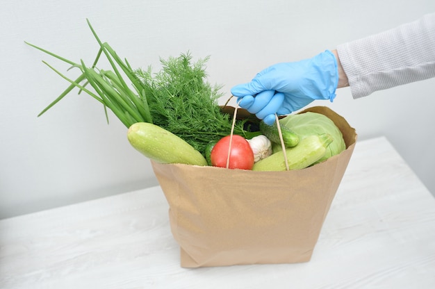 Voluntario en guantes azules pone un paquete de verduras sobre la mesa. paquete de donación de alimentos vegetales