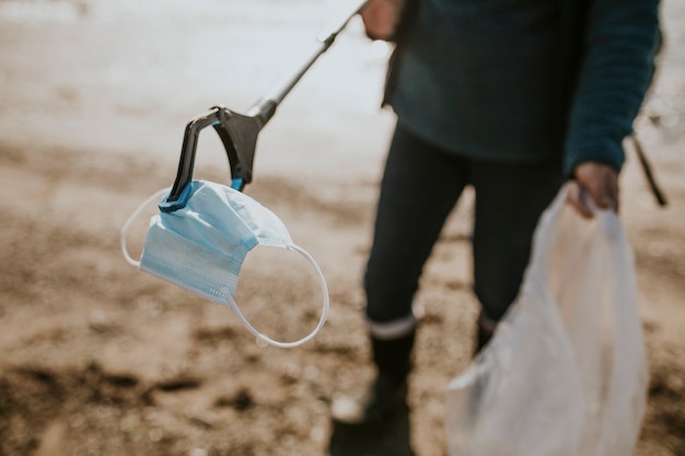 Voluntario de limpieza de playa recogiendo mascarilla para campaña ambiental