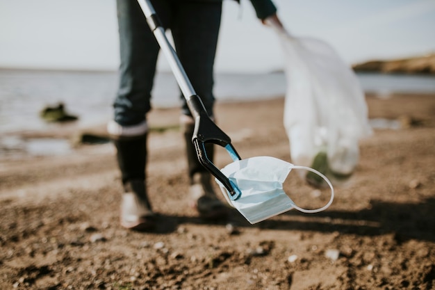 Voluntario de limpieza de playa recogiendo mascarilla para campaña ambiental