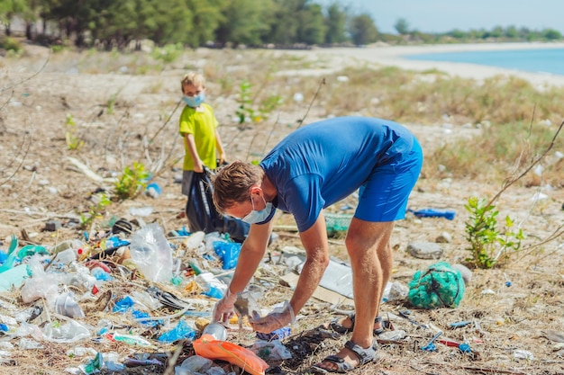 Voluntario mascarilla azul bosque arena playa Hijo ayuda a padre a sostener una bolsa negra para recoger basura Problema basura derramada basura planeta contaminación protección ambiental Educación infantil natural
