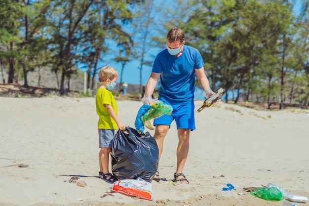 Voluntario mascarilla azul bosque arena playa Hijo ayuda a padre a sostener una bolsa negra para recoger basura Problema basura derramada basura planeta contaminación protección ambiental Educación infantil natural