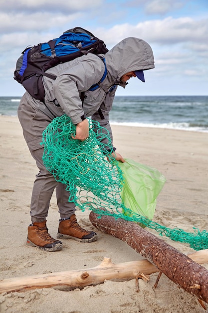 Voluntário masculino coleta lixo jogado por uma tempestade em uma praia arenosa em tempo ventoso