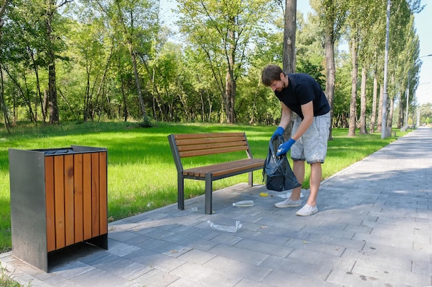 Un voluntario masculino recoge desechos plásticos en una bolsa negra en un parque público. Problemas ambientales