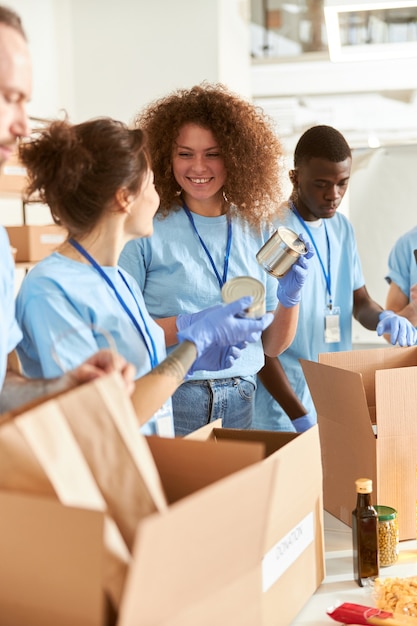 Voluntarios alegres en guantes protectores clasificando el embalaje de alimentos enlatados en cajas de cartón trabajando