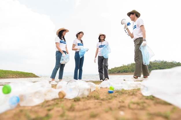 Voluntários da comunidade jovem asiática usando sacos de lixo para limpar a natureza