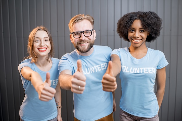 Voluntarios felices en camisetas azules que muestran el signo de OK en la oficina