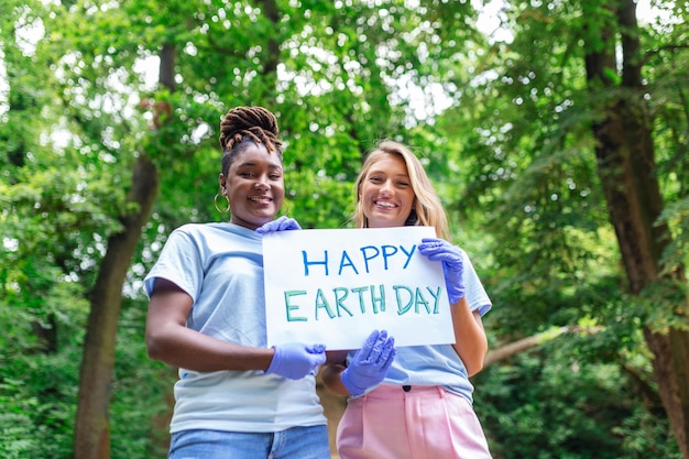 Voluntarios felices sosteniendo un cartel con el mensaje "feliz día de la Tierra" Voluntariado caritativo limpiando personas y concepto de ecología grupo de voluntarios felices con bolsas de basura limpiando el área en el parque