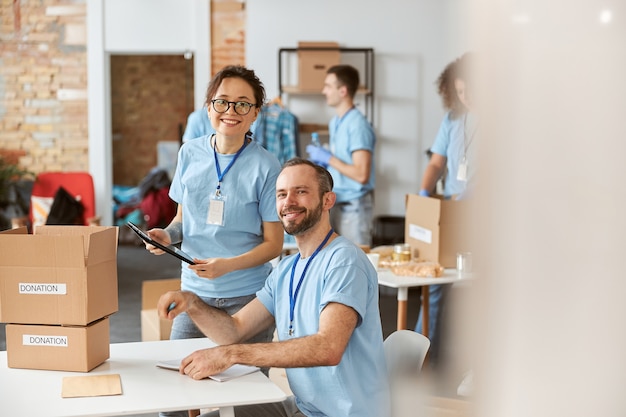 Voluntarios de hombre y mujer sonriendo a la cámara felices de trabajar juntos en un proyecto de donación en el interior