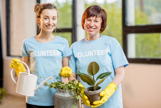 Voluntarios jóvenes y mayores vestidos con camisetas azules cuidando plantas verdes en el interior