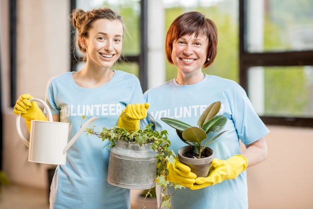 Voluntários jovens e mais velhos vestidos com camisetas azuis cuidando das plantas verdes dentro de casa