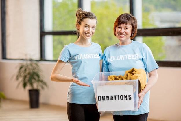 Voluntários jovens e mais velhos vestidos com camisetas azuis segurando um recipiente com doações de roupas dentro do escritório