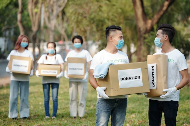Voluntarios con máscaras médicas que llevan cajas de cartón y paquetes llenos de ropa y comestibles donados para personas sin hogar