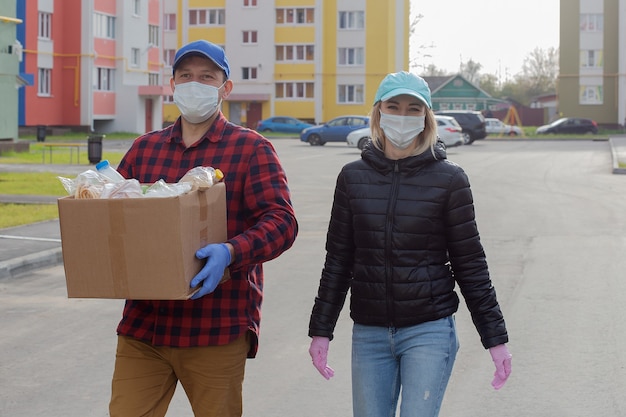 voluntarios con máscaras protectoras con una caja de comida, caminan por la calle