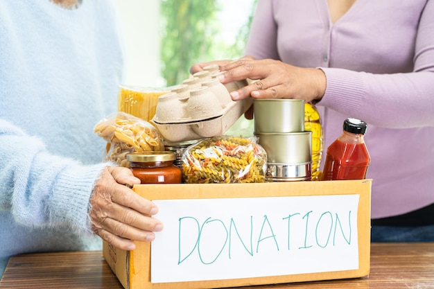 Voluntarios poniendo varios alimentos secos en una caja de donaciones para ayudar a las personas.