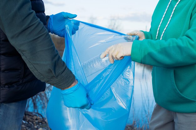 Los voluntarios recogen botellas de plástico en bolsas, primer plano de las manos, el concepto de ecología y protección de la tierra.