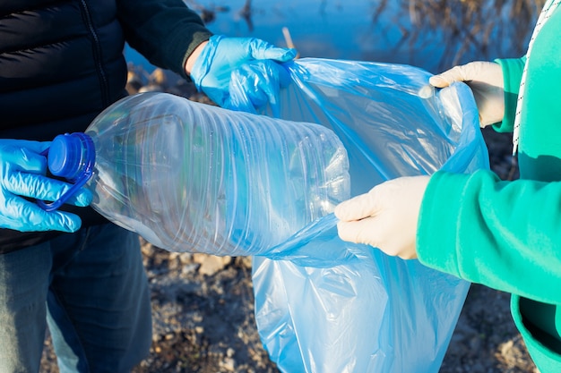 Voluntários recolhem garrafas plásticas em sacos, close-up das mãos, conceito de ecologia e proteção da terra.