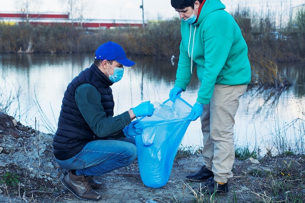 Voluntários recolhem garrafas plásticas em sacos na margem do rio, pelo conceito de ecologia e proteção do solo.