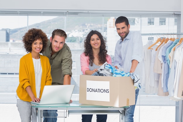 Voluntarios usando una computadora portátil y tomando ropa de una caja de donación