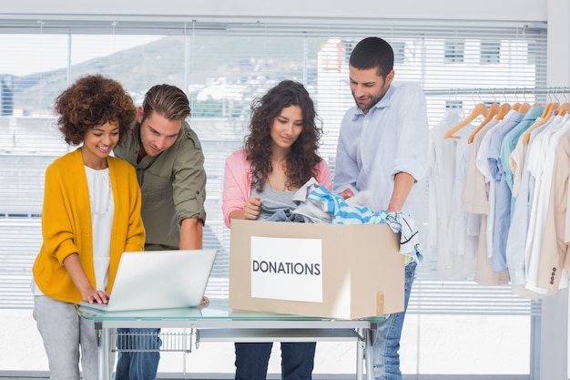 Voluntarios usando una computadora portátil y tomando ropa de la caja de donaciones