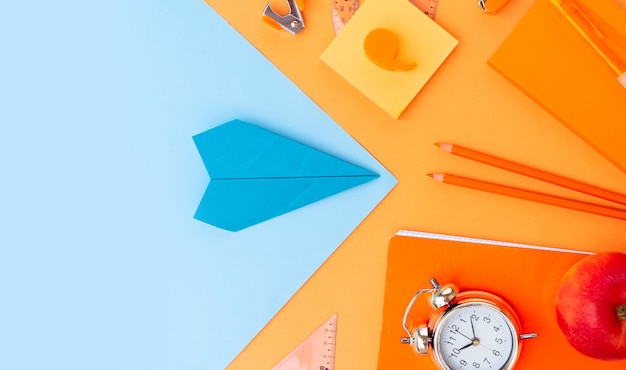 Volver al borde de la vista superior de estilo escolar con útiles escolares y avión de papel sobre fondo naranja, vista superior