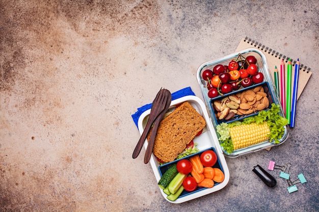 Volver al concepto de escuela. Caja de almuerzo con alimentos frescos y saludables. Sándwich, verduras, frutas y nueces en un recipiente de comida, fondo oscuro.