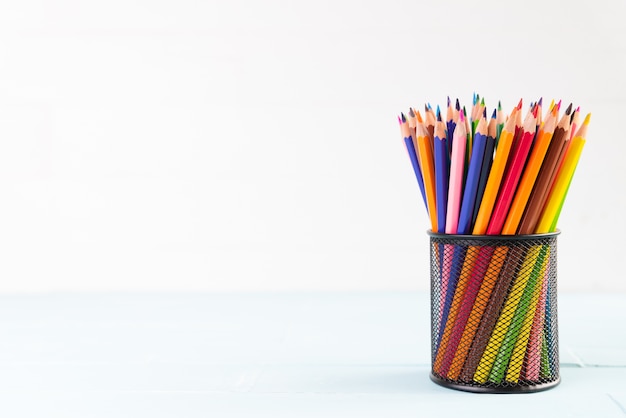 Volver al concepto de escuela, lápices de colores en caja sobre fondo blanco de madera.