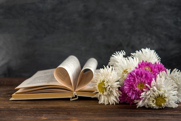 Volver al concepto de escuela. Libro y flores astra en tablero negro. 1 de septiembre día.