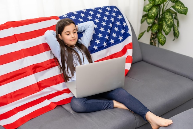 Volver a la educación escolar en línea. Difícil hablar inglés. Niño haciendo la tarea en la computadora. Estudiante que estudia en la computadora portátil sobre la bandera estadounidense. Tutor enseña a distancia.