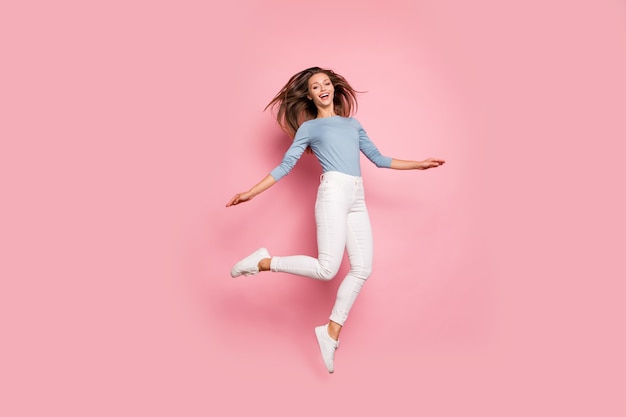 Volvió la foto del tamaño del cuerpo de longitud completa de la alegre niña bonita linda positiva saltando con zapatillas de deporte aislado fondo de color pastel