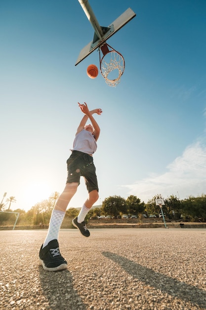 Vom Boden aus spielt ein energiegeladenes Kind auf dem Platz Basketball und übt an einem sonnigen Tag das Werfen in den Korb