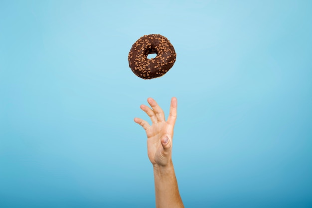 Von Hand einen Donut mit Schokoladenglasur fangen. Blauer Karton. Konzept des Backens, handgemacht. Flache Lage, Draufsicht