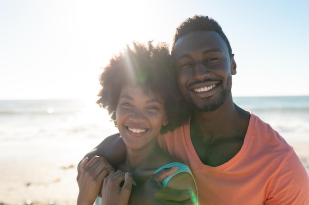 Von hinten beleuchtetes Porträt eines lächelnden afroamerikanischen Paares, das an einem sonnigen Tag den Sommerurlaub am Strand genießt