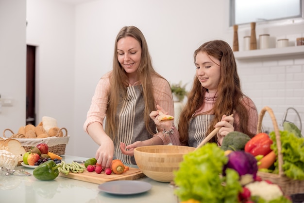 Von ihrer Mutter lernt ein junges Mädchen, wie man ein Abendessen zubereitet. gesunde Mahlzeiten zubereiten. In der Küche eine glückliche Familie. Das Gemüse und das Obst werden von der Mutter und ihrer Tochter zubereitet.