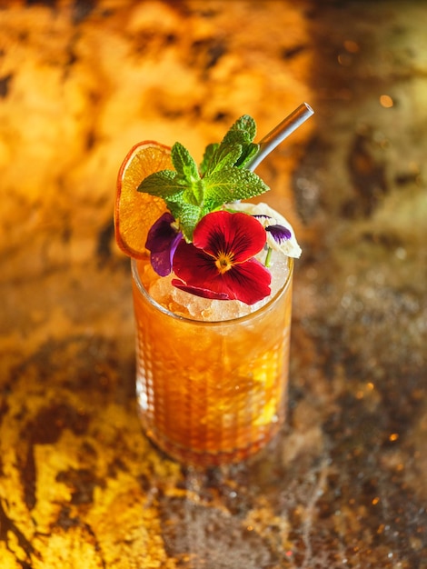 Von oben aus aus Glas mit alkoholischem Langgetränk Cocktail geschmückt mit essbaren Blumen und getrockneten Orangen serviert an der Theke der Bar