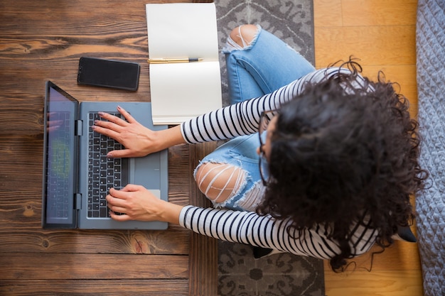 Von oben geschossen, sitzt ein junges schönes Mädchen in ihrem Wohnzimmer und benutzt ihren grauen Computer