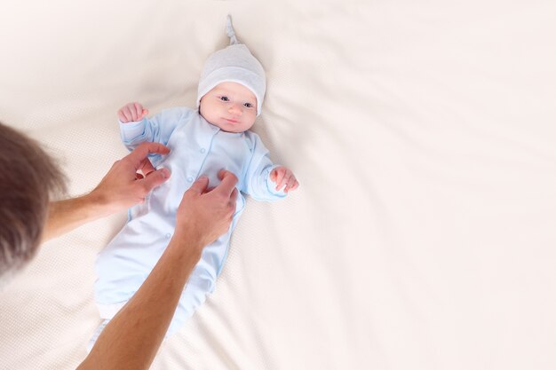 Von oben von Papas Händen, die das kleine Baby zu Hause verkleiden. Vaterschaft Konzept.