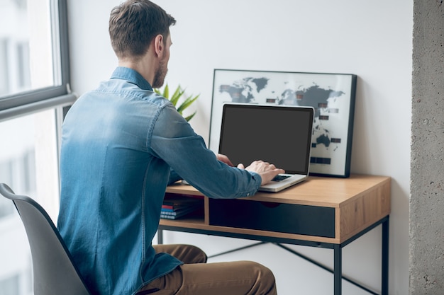 Von zuhause aus arbeiten. Dunkelhaariger Mann, der am Tisch sitzt und an einem Laptop arbeitet